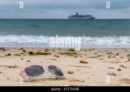 Plastic Pollution: Dropped sunglasses with cruise ship in the background. Bournemouth, UK. Stock Photo