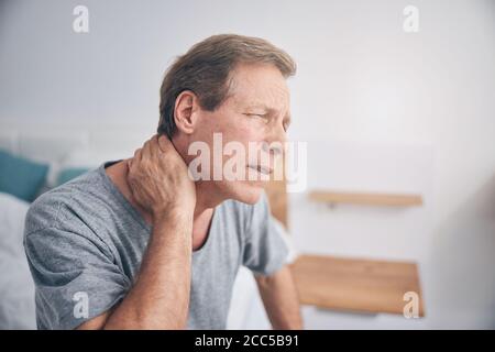 Upset mature man suffering pain in neck Stock Photo