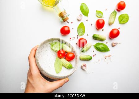 Fresh cut salad ingredients falling into white bowl on white minimal background. Ingredients for making dieting healthy vegetable salad. Stock Photo