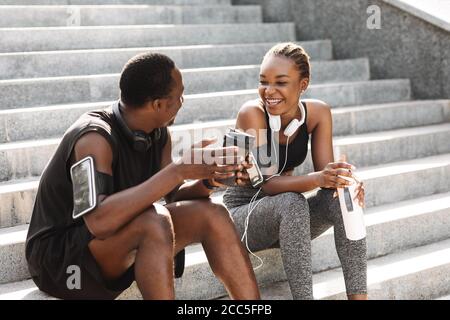 Fit Black Couple Taking Rest After Workout Outdoors, Sitting On Urban Stairs Stock Photo