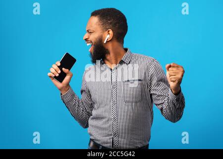 Happy afro man singing using smartphone as mic Stock Photo