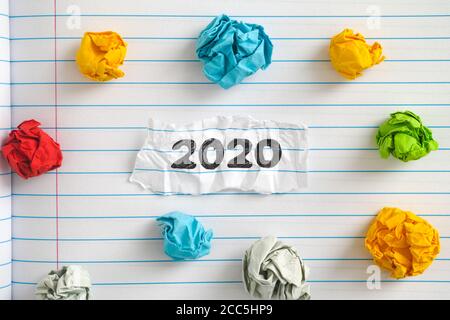 The year 2020. A piece of paper with the year 2020 written on it on a notebook sheet with some colorful crumpled paper balls around it. Close up. Stock Photo