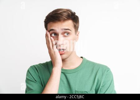 Image of puzzled caucasian man in basic t-shirt being stressed and grabbing his face isolated over white background Stock Photo
