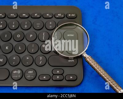 Closeup overhead POV shot of a traditional magnifying glass over the enter key on a computer keyboard. Stock Photo