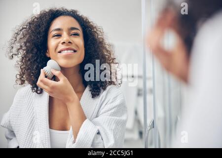 Pleased young woman performing an exfoliation procedure Stock Photo