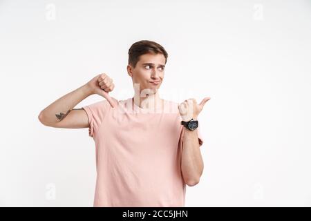 Image of confused caucasian man in basic t-shirt showing thumb down and pointing finger aside isolated over white background Stock Photo