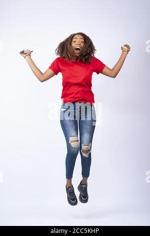 happy young african lady jumping in excitement, holding her phone Stock Photo