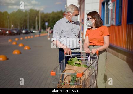 Senior couple with face masks and shopping walking outside supermarket Stock Photo