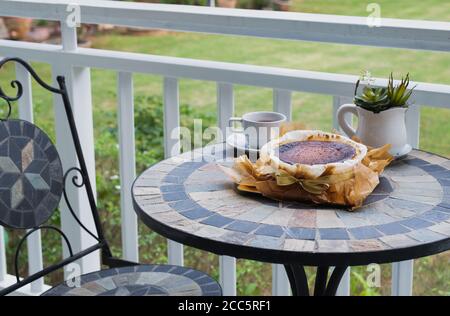 Basque burnt cheesecake with cup coffee on table on balcony with garden view. Stock Photo