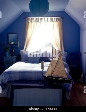 Divan bed and dressing table in small attic room painted blue Stock Photo