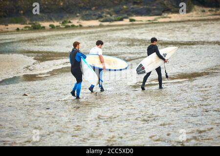 People walking with surf boards on Perranporth beach in Cornwall on Christmas Day Stock Photo