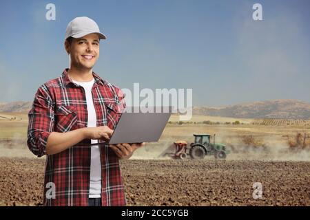 Agricultural engineer in a field with a laptop computer and a tractor plowing the soil Stock Photo