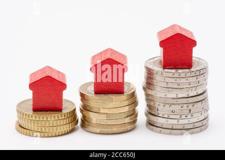 Three stacks of euro coins with red arrow-shaped houses on top, white background Stock Photo