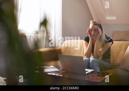 Stressed young woman working from home on sofa in living room Stock Photo