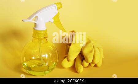 Yellow rubber gloves and a plastic spray bottle for detergent on a yellow background Stock Photo