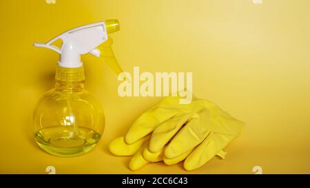 Yellow rubber gloves and a plastic spray bottle for detergent on a yellow background Stock Photo