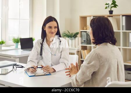 Young smiling doctor therapist listening to patients complaints and making notes in clinic Stock Photo