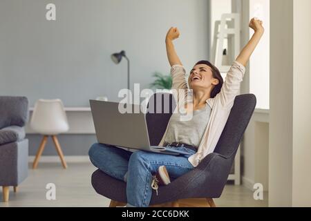 Positive young girl with laptop stretching in cozy armchair after work. Beautiful businesswoman relaxing at home office Stock Photo