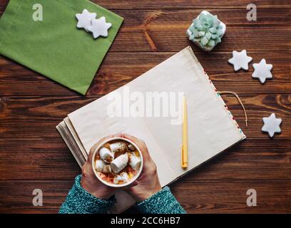 Female hands holding coffee with marshmallow on rustic wooden table Stock Photo