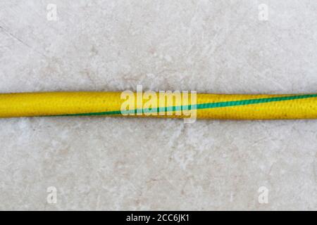 Yellow and green colored old hose on the ground. Yellow and green old hose. Old garden hose close-up. Stock Photo