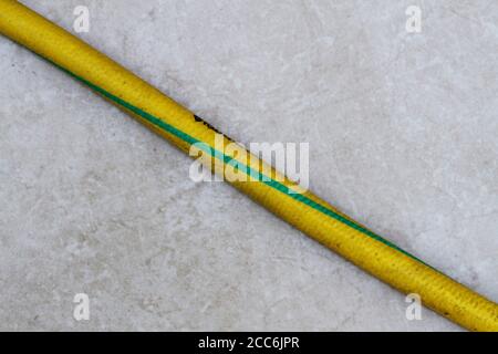 Yellow and green colored old hose on the ground. Yellow and green old hose. Old garden hose close-up. Stock Photo