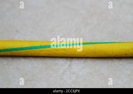 Yellow and green colored old hose on the ground. Yellow and green old hose. Old garden hose close-up. Stock Photo