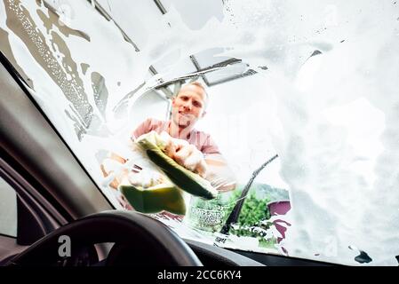 Car washing process: man washes front car window with soap Stock Photo
