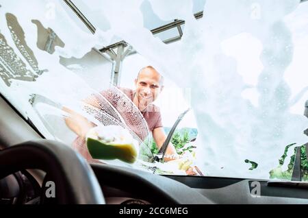 Man washes his car front window inside the car camera view Stock Photo