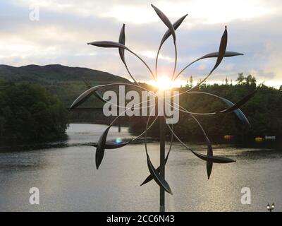 Seen through a wind sculpture created by Lyman Whitaker, the sun is setting over Loch Faskally in Piltochry; Scotland, August 2020 Stock Photo
