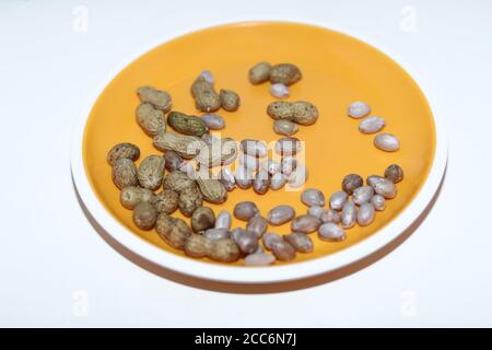 Peanuts in shells on yellow background. Raw peanuts top view isolated on yellow plate backgrounds Stock Photo