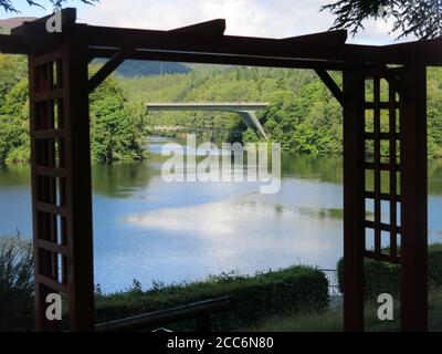 Framed by a latticed pergola, a view overlooking Loch Faskally in Highland Perthshire with the road and pedestrian bridges to Pitlochry. Stock Photo