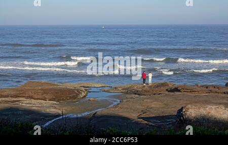Two women stand on a rocky overlook above the Pacific Ocean on an ocean path in the small town of Yachats, Oregon. Stock Photo