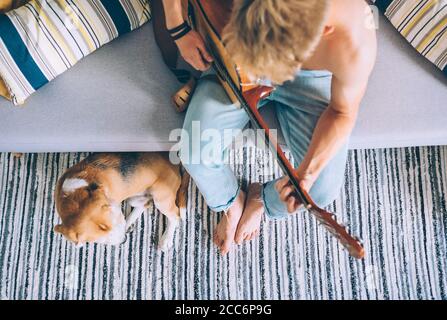Young man plays on guitar sitting on sofa in cozy home Stock Photo
