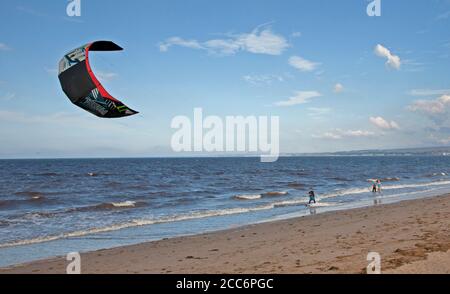 Portobello, Edinburgh, Scotland, UK. 19 August 2020. Windy afternoon blew the haze away which persisted in the morning with scattered spells of sunshine later. Wind 22 km/h with potential gusts of 42 km/h assisting this Kite Surfer. Stock Photo