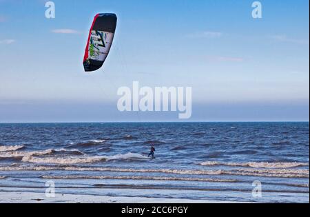 Portobello, Edinburgh, Scotland, UK. 19 August 2020. Windy afternoon blew the haze away which persisted in the morning with scattered spells of sunshine later. Wind 22 km/h with potential gusts of 42 km/h assisting this Kite Surfer. Stock Photo