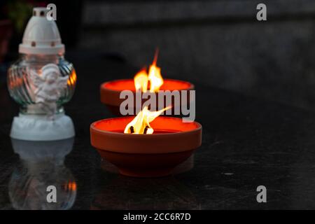 Traditional burning grave candles and decorative one on a black marble grave during All Souls' Day with copy space Stock Photo