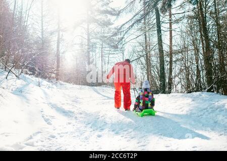 Father carries the sled with his little daughter on the snow slope in winter forest Stock Photo