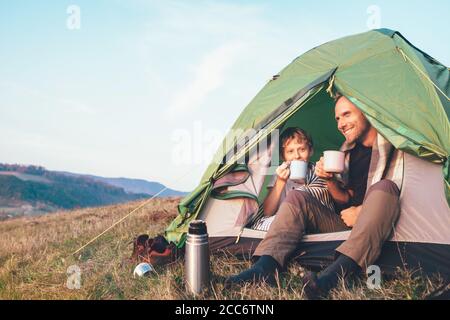 Family lisure concept image. Father and son drink a tea sitting in touristic tent Stock Photo