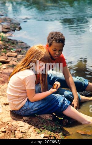 1970s 1980s TWO PRETEEN KIDS CAUCASIAN GIRL AND AFRICAN-AMERICAN BOY WEARING BLUE JEANS SITTING FEET IN WATER PLAYING IN STREAM - 065535 TAY001 HARS FRIENDSHIP HALF-LENGTH STONES STREAM MALES DENIM MIXED PRETEEN BOY HIGH ANGLE ADVENTURE DISCOVERY AFRICAN-AMERICANS AFRICAN-AMERICAN AND RECREATION REDHEAD BLACK ETHNICITY CURLY IN BAREFOOT PRETEEN ROCKS RED HAIR VARIOUS VARIED BLUE JEANS CHILDHOOD JUVENILES MIXED RACE PRE-TEEN PRE-TEEN BOY PRE-TEEN GIRL TOGETHERNESS CAUCASIAN ETHNICITY INNOCENT OLD FASHIONED AFRICAN AMERICANS Stock Photo