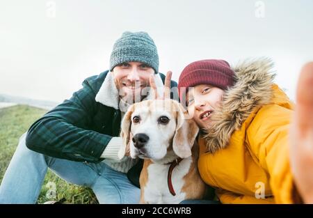 Father and son dressed in warm clothes taking a selfie photo with their best family member beagle dog. Stock Photo