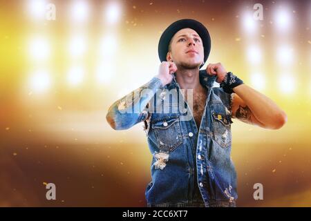 Jeans dressed Dancer teenager man in denim jacket posing on the dance stage with bright spotlights background. Stock Photo
