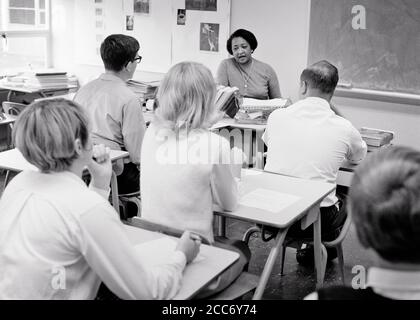 1960s BACKS OF ANONYMOUS ADULT STUDENTS IN CLASSROOM BEING TAUGHT BY A MATURE AFRICAN-AMERICAN WOMAN TEACHER SPEAKING LECTURING - s15984 HAR001 HARS MALES CONFIDENCE B&W DESKS GOALS SCHOOLS AFRICAN-AMERICANS AFRICAN-AMERICAN INSTRUCTOR KNOWLEDGE LEADERSHIP BLACK ETHNICITY REAR VIEW HIGH SCHOOL OCCUPATIONS HIGH SCHOOLS EDUCATOR ANONYMOUS BACK VIEW COOPERATION EDUCATING EDUCATORS INSTRUCTORS MID-ADULT MID-ADULT WOMAN SCHOOL TEACHES TOGETHERNESS BLACK AND WHITE CAUCASIAN ETHNICITY HAR001 OLD FASHIONED AFRICAN AMERICANS Stock Photo