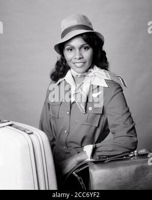 1970s SMILING AFRICAN-AMERICAN WOMAN AIRLINE STEWARDESS POSED WITH LUGGAGE HANDBAG WEARING HAT LOOKING AT CAMERA - s20923 HAR001 HARS CAREER YOUNG ADULT SAFETY PLEASED JOY LIFESTYLE AIRLINE FEMALES JOBS HEALTHINESS COPY SPACE HALF-LENGTH LADIES PERSONS PROFESSION CONFIDENCE TRANSPORTATION EXPRESSIONS B&W EYE CONTACT SKILL OCCUPATION HAPPINESS SKILLS WELLNESS CHEERFUL ADVENTURE STRENGTH CUSTOMER SERVICE AFRICAN-AMERICANS AFRICAN-AMERICAN CAREERS KNOWLEDGE BLACK ETHNICITY PRIDE AUTHORITY OCCUPATIONS SMILES CONCEPTUAL JOYFUL STYLISH COMPETENT FLIGHT ATTENDANT POSED STEWARDESS YOUNG ADULT WOMAN Stock Photo