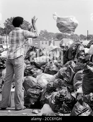 1970s AFRICAN-AMERICAN MAN TOSSING A TRASH BAG ON LARGE PILE OF ACCUMULATED TRASH BAGS DURING A CITY GARBAGE COLLECTION STRIKE - s21167 HAR001 HARS AFRICAN-AMERICANS AFRICAN-AMERICAN STRIKE BLACK ETHNICITY A OF ON CONCEPTUAL TOSSING RUBBISH YOUNG ADULT MAN BLACK AND WHITE DURING HAR001 OLD FASHIONED REFUSE AFRICAN AMERICANS Stock Photo