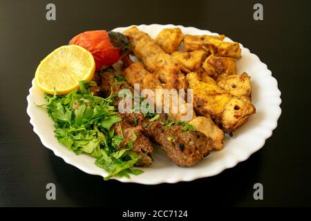 Famous traditional Arabic, Turkish, Israel food. Grilled chicken shashlik, lamb, beef kofta kebab, vegetables, lemon on white plate on dark wooden bac Stock Photo