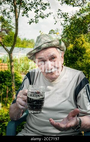 Portrait of a handsome elderly man of 87 years old, drinking a cool drink in the garden after work. Happy active old age. A man drinks dark beer Stock Photo