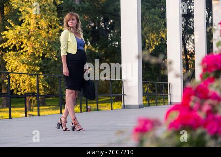 A smiling pregnant caucasian woman posing in front of a modern building. Stock Photo