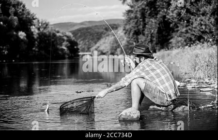I catch it by myself. bearded man with fish on rod. hipster fishing with spoon-bait. fly fish hobby. Hipster in checkered shirt. successful fisherman in lake water. big game fishing. relax on nature. Stock Photo
