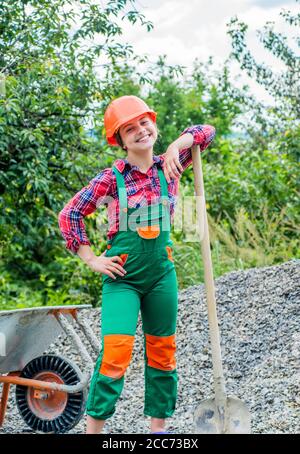tired construction work. girl builder takes a shovel of rubble. hardworking youth. game of builder and construction. Outdoor activity concept. girl who is transporting rubble in a wheelbarrow. Stock Photo