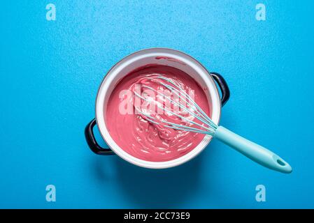 Melted Ruby chocolate in a pot, isolated on a blue background. Top view of a pot of Belgian pink chocolate melt. Preparing sweet food. Home cooking. Stock Photo